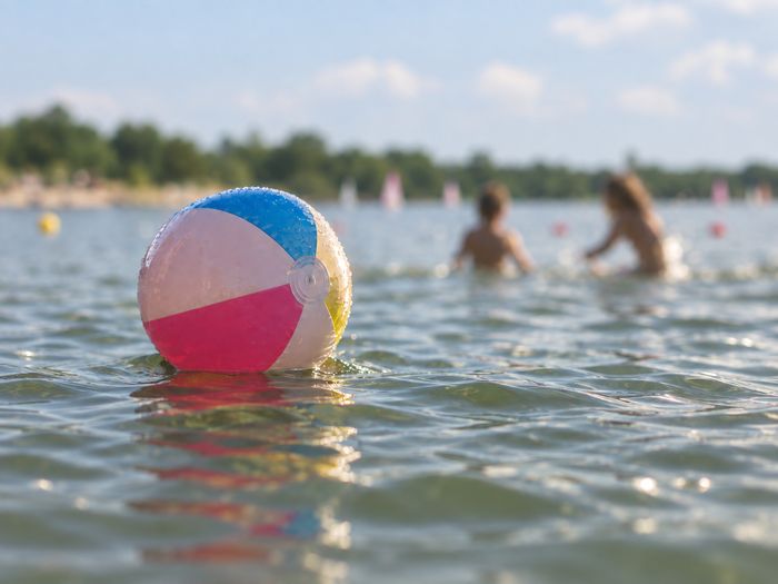 Ballon flottant à la surface du plan d’eau de Reiningue, avec des silhouettes floues de baigneurs à l’arrière-plan