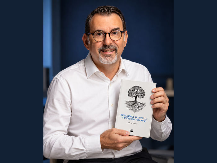 Portrait d’Olivier Grenet tenant son essai Intelligence artificielle et évolution humaine