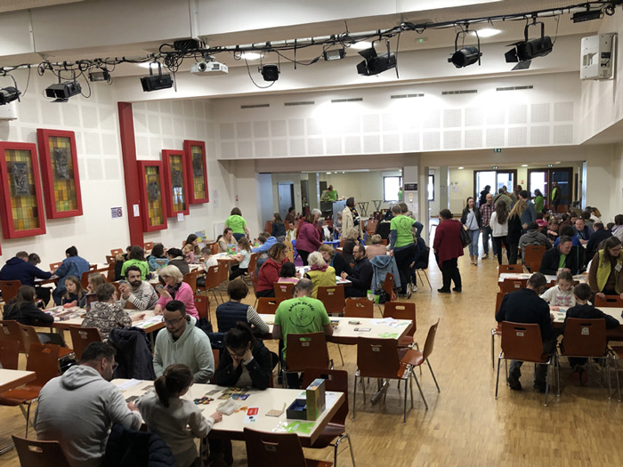 Vue d’ensemble du Salon du jeu Jeukado à Sigolsheim, avec des familles et des joueurs réunis autour des tables de jeux de société.
