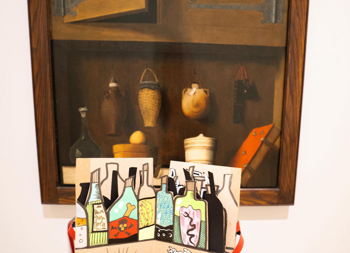 Carnet d’illustrations colorées représentant des flacons, présenté devant une vitrine du musée Unterlinden à Colmar